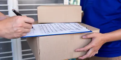 Pessoa recebendo encomenda e assinando comprovante de entrega sobre uma caixa de papelão, representando processo de logística e confirmação de recebimento.